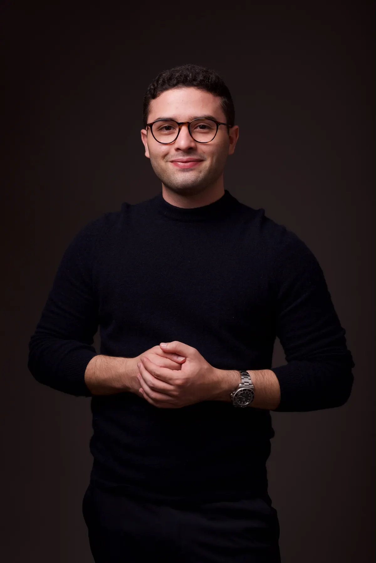 Dr. Gabriel Nogueira, de suéter preto, sorrindo, com as mãos entrelaçadas